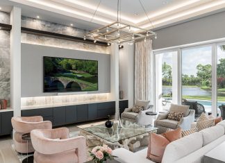 The great room’s tranquil palette, organic forms, and linear architectural details create an elevated living experience designed to bring the family together. A creamy white EJ Victor sofa combines with plush pink chairs and soft gray occasional chairs, all from Sam Moore. The marble-clad entertainment center takes center stage along with a stunning Currey & Company chandelier.
