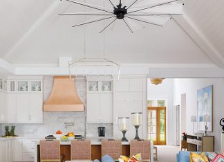 An oversized ceiling fan punctuates the peaked ceiling over the open kitchen, great room, and dining area. White cabinetry and a gleaming copper range hood complement the great room’s blue O. Henry House sofas and multi-colored Pierre Frey and Quadrille pillow fabrics.