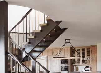 A grand entrance marked by a circular staircase creates a dynamic architectural element visible from the dining area. The entry rug introduces a touch of pattern to the home’s calming, neutral palette. Lexington’s clean-lined dining table and chairs pair exceptionally with a linear statement chandelier from Ashore.