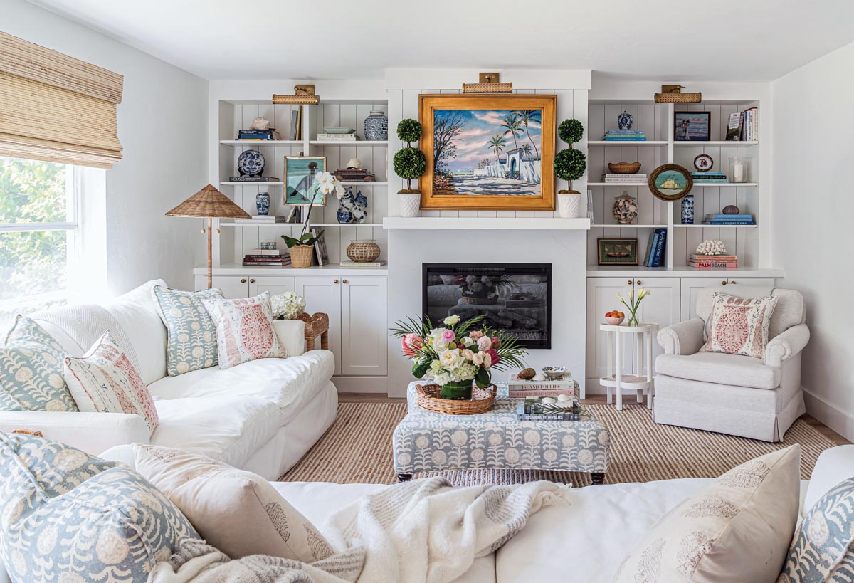 Books, sea treasures, porcelain ceramics, and vintage decor line the built-in shelves in the living room. The Paul Arsenault painting above the mantle provided some inspiration for the home&rsquo;s color palette, including the Penny Morrison block print textiles found throughout the room.