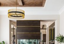 In front of the custom fireplace, a small seating area with four club chairs by Chaddock Home provides a cozy conversation area. The brass chandelier is by Arteriors Home. “We wanted to give the homeowners a few areas in the home that were dressier by adding in brass and the warm tones,” says interior designer Kendall Schulte Hannon. “Then we juxtaposed those elements with the bright citrine yellow stools.”