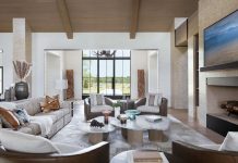 Country Cachet in Okeechobee Family Home The living room’s double-sided fireplace—shared with an adjacent club room—generates a sculptural centerpiece, lending warmth and ambiance while maintaining an open-concept layout. A sizable sofa from Lazar Industries and cozy Century club chairs establish a conversation area around a trio of marble-topped Palecek cocktail tables.