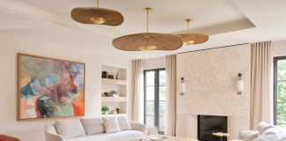 The living room features a coral stone fireplace accented with fine fluting at the lower portion for textural appeal. Built-in shelves flank the artwork centered behind a Poltrona Frau sofa. The abstract painting inspired the subtle orange hues of a pair of Avenue Road lounge chairs and the gold-finished rattan pendants by Hudson Valley Lighting.