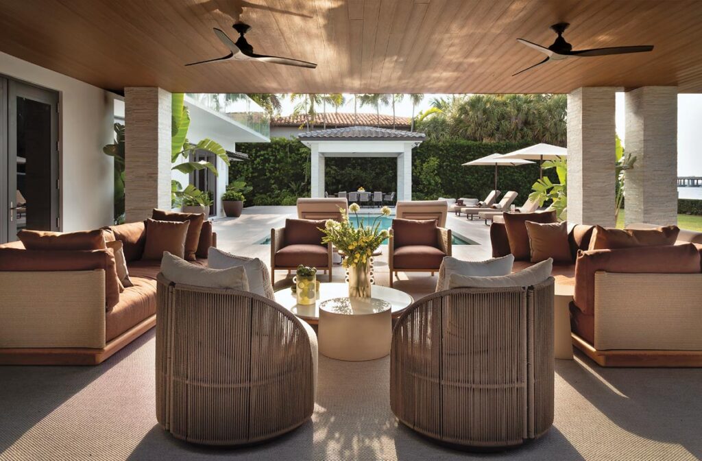 A covered terrace features a wood-clad ceiling that shelters outdoor seating from Kettal and Harbour selected for its playful forms and rich textures. Chosen in warm, earthy tones, the pieces complement the surrounding greenery and waterfront views while allowing the architecture to remain the focal point.
