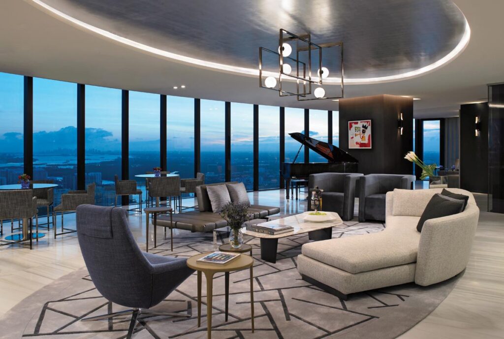 A study in geometric harmony, the light-filled entertainment salon lets oval forms rule the day. Echoing the building’s curved walls, a sofa sits atop a custom-designed oval area rug whose linear patterns flawlessly mirror the architectural inset lighting and the dramatic chandelier above. A piano stands ready for regular celebrations.