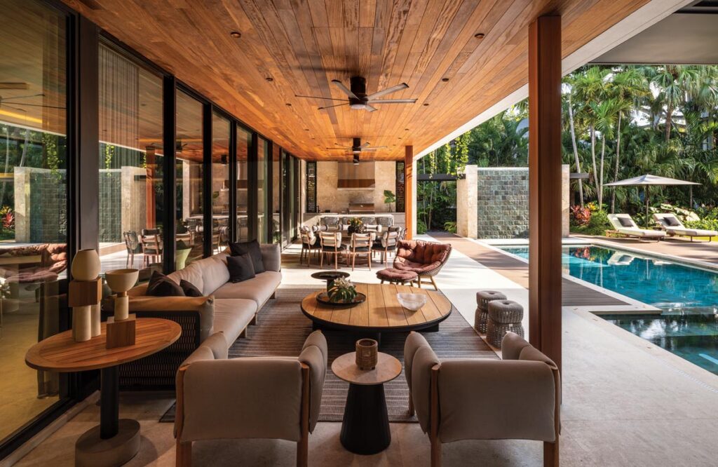 Designed for year-round entertaining, the outdoor living area features direct access to the pool terrace and surrounding gardens. A covered lounge grouping includes seating pieces from Kettal, Dedon, and Poltrona Frau. An adjacent dining space outfitted with Kettal furnishings and island stools complements a fully equipped outdoor kitchen.