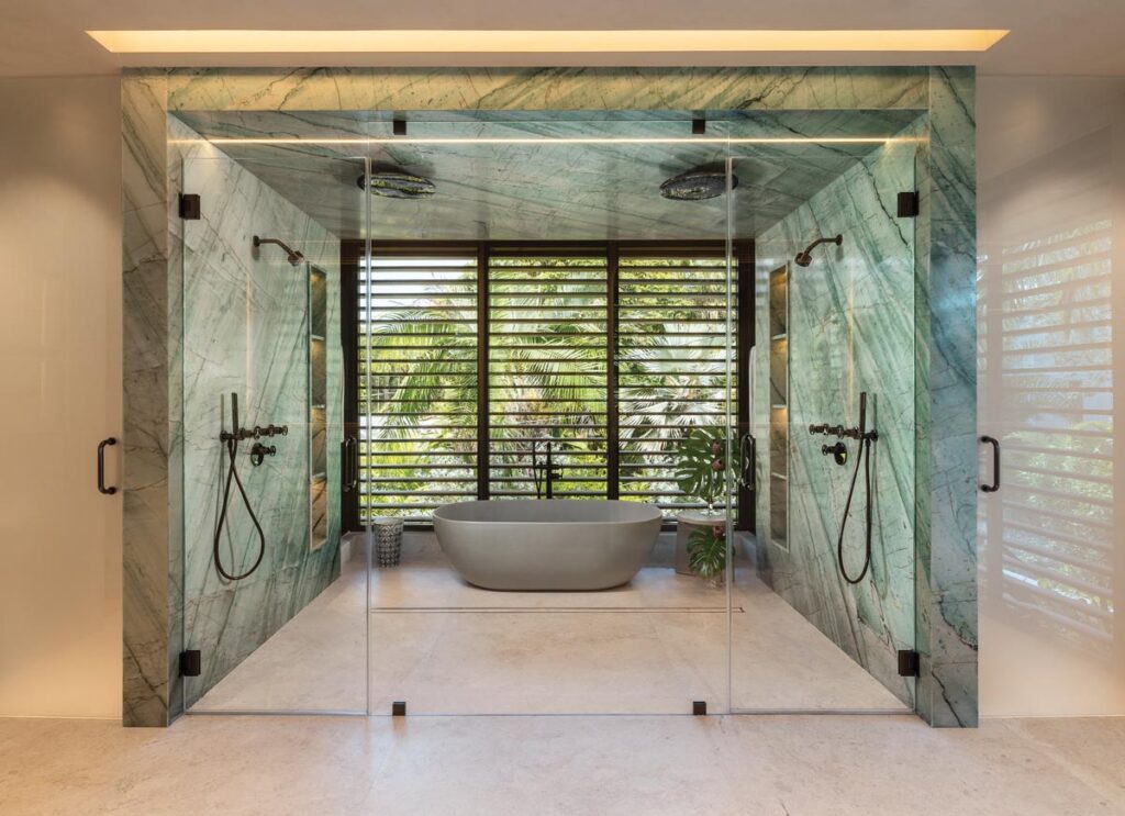 Dramatic green marble slabs from Doral Stones envelop the shower enclosure and bathing area, creating a striking focal point while reinforcing the home’s emphasis on natural materials and timeless design.