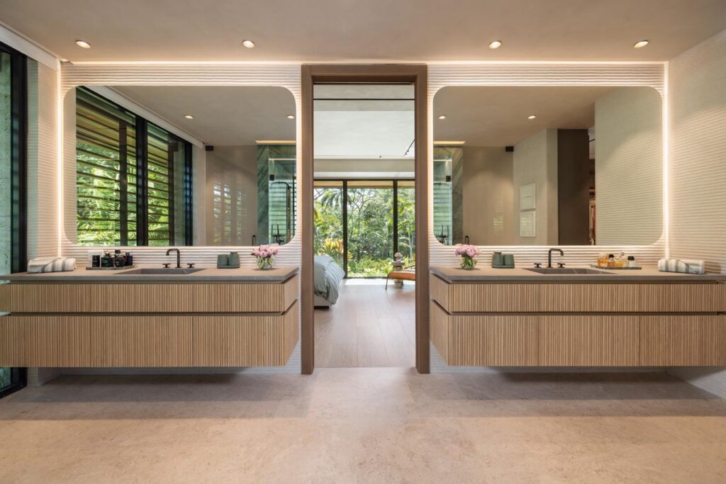 Floating double vanities from MiaCucina visually connect to the bedroom, contributing to the serene, spa-like atmosphere of the primary suite. Integrated ambient lighting, natural sunlight, curated finishes, and views of the surrounding greenery instill a sense of calm.
