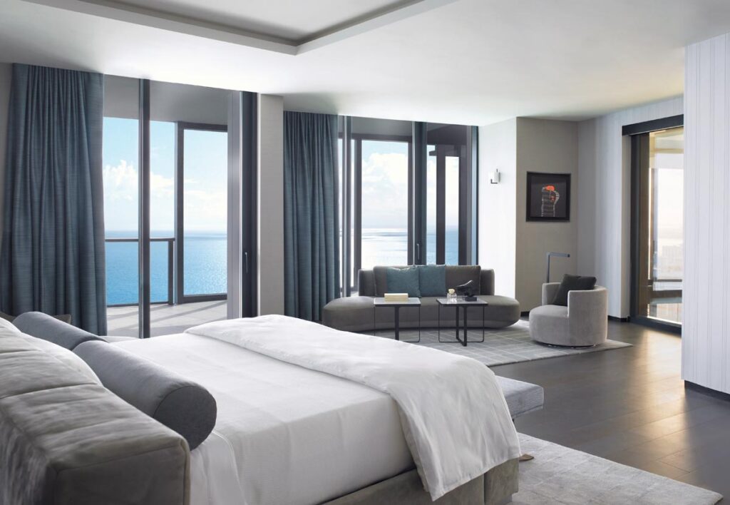 In the primary suite, a sophisticated, intentional greige palette allows the vibrant coastal horizon to remain the absolute focal point. Wolk composed a fluid, floating arrangement using a Smartline bed and coordinating sofa, complemented by an elegant round Addison House chair and sleek accent tables. A bespoke bench by Carriage House mirrors the structural curve of the architecture.