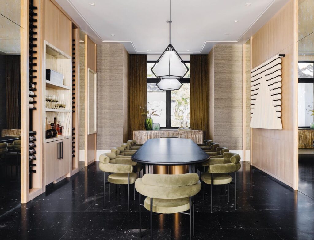 Nero Marquina marble flooring anchors the dining room and serves as a contrast to other textures, mainly the custom wallcovering and blond oak millwork. Nuevo Living chairs upholstered in green velvet surround a dining table by Made by Moniomi. Pendants by Gabriel Scott introduce a slight industrial vibe in the room.