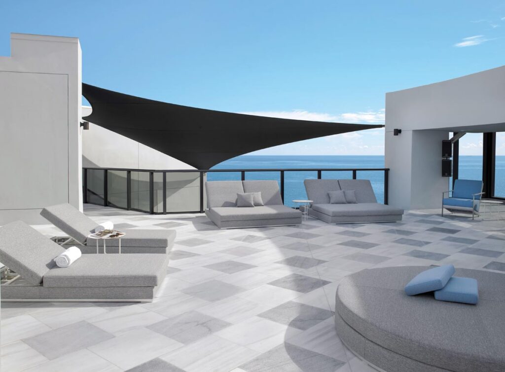 The rooftop pool deck serves as the ultimate perch for high-profile entertaining. Streamlined chaise lounges and side tables from Casa Design Group offer refined spaces for relaxation, while a striking periwinkle blue chair by Wolk anchors the layout.