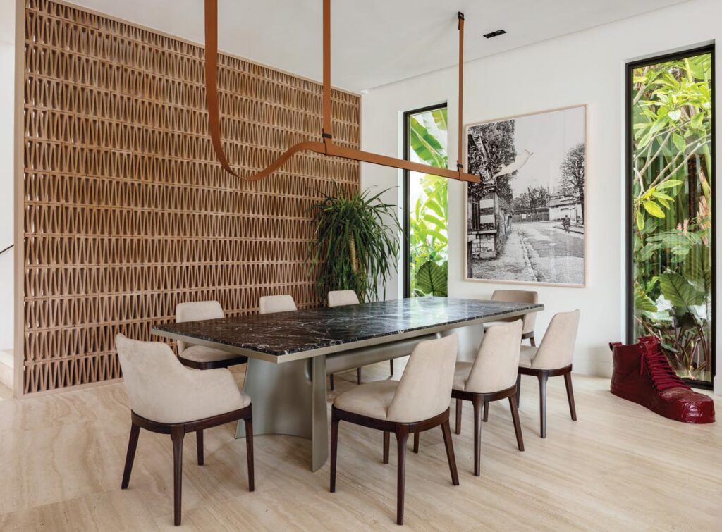 The dining room’s breeze-block wall forms an architectural feature that screens the staircase while introducing a dynamic play of light and shadow. Poliform’s marble dining table and custom taupe suede chairs are illuminated with a sculptural Flos lighting fixture. Jose Dávila’s photographic artwork counterbalances a conversation-sparking sneaker sculpture by one of the homeowners’ children.