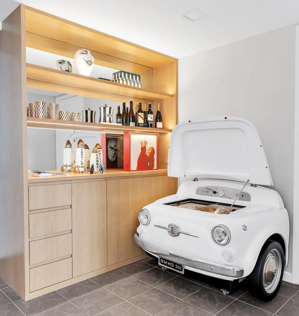 The bar area of the apartment features light oak millwork that houses all sorts of cocktail accoutrements. The wall-mounted beverage cooler (officially known as the SMEG500) is from a 2013 collaboration between Fiat and Smeg.