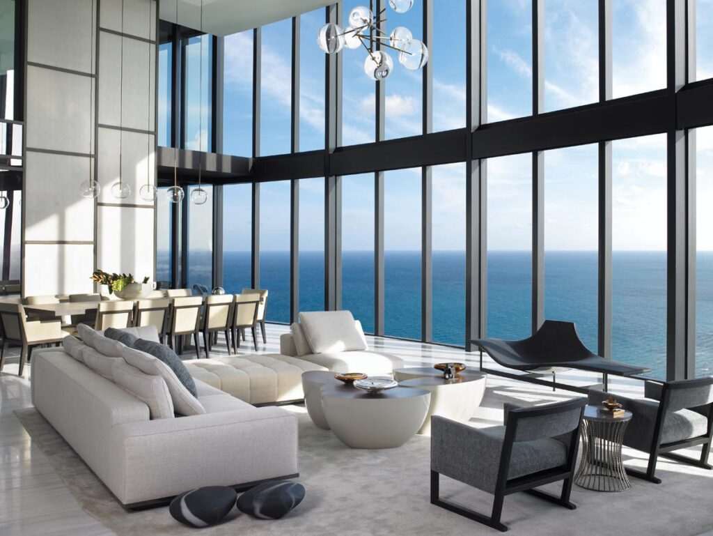 To balance the immense volume of the 20,000-square-foot residence’s main salon, designer Michael Wolk paired tailored Minotti seating with Maxalto chairs and a sculptural black Luminaire bench. The homeowners’ personal cocktail table anchors the central grouping, while in the background, a massive 12-person dining table from David Sutherland commands the room beneath a striking Smartline chandelier.