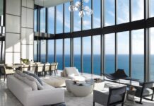 Modernist Grandeur in a Sunny Isles Beach Penthouse To balance the immense volume of the 20,000-square-foot residence’s main salon, designer Michael Wolk paired tailored Minotti seating with Maxalto chairs and a sculptural black Luminaire bench. The homeowners’ personal cocktail table anchors the central grouping, while in the background, a massive 12-person dining table from David Sutherland commands the room beneath a striking Smartline chandelier.