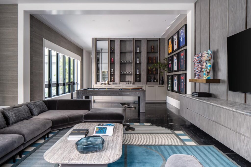 Unlike some of the more formal spaces in the residence, the game room was designed to feel more relaxed and personal. “We leaned into a deeper, moodier palette with rich charcoal tones, and textured materials,” says Alvarez. “The architectural lines were balanced with soft upholstery and curated objects.” The framed basketball jerseys on the wall are part of the husband’s sports memorabilia collection.