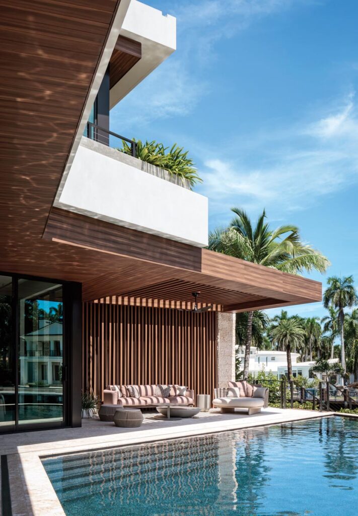 What appears to be richly toned timber throughout the exterior and covered outdoor spaces is actually Covet architectural metal, an engineered aluminum that resembles natural wood while offering far superior durability. On the pool terrace, an intimate lounge seating group from Kettal, upholstered in striped blush-and-cream fabric, offers respite beneath the loggia’s slatted ceiling.