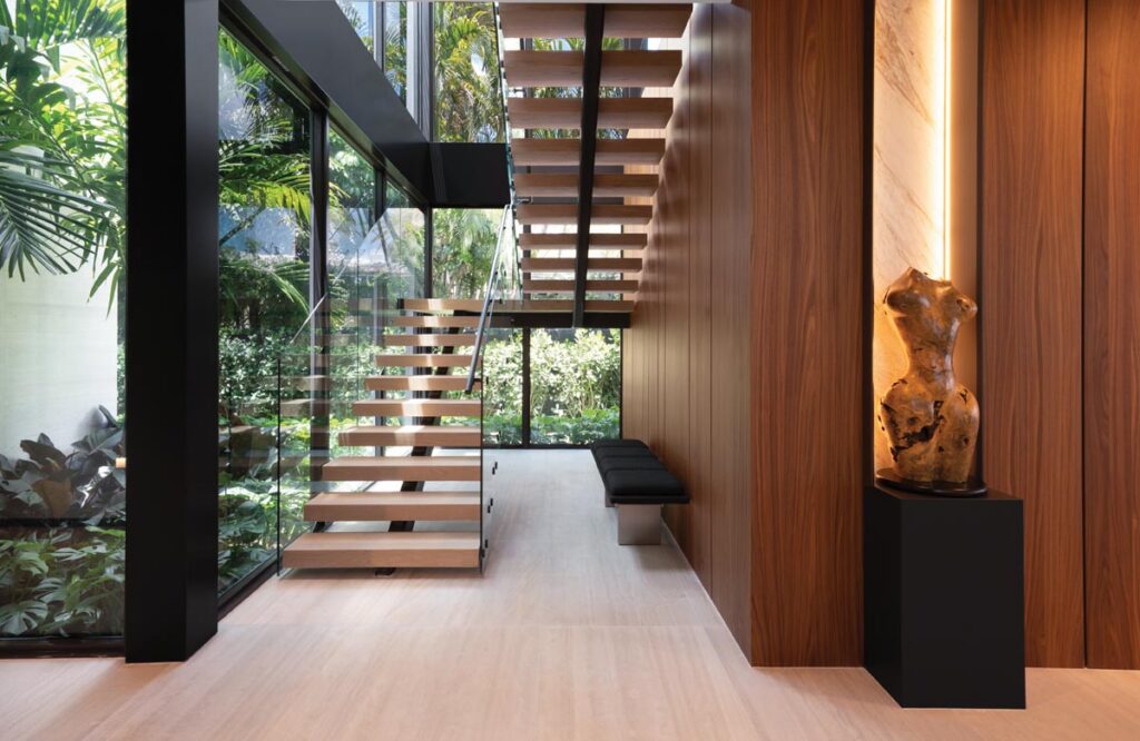 A staircase—part of which features glass on one side and warm timber on the other—creates a moment of compression before the upper level opens to sky and water.