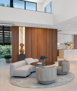 An intimate conversation area near the staircase lends a warm welcome with a curved sofa and swivel chairs from Minotti gathered around a Bellagio lounge table. A plush area rug from Vesta Home anchors the grouping.