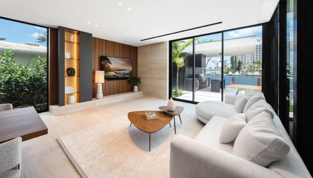 At the waterfront end of the ground floor, the family room offers a cozier scale, drawing the eye directly to the water view. This is the space where the house exhales with Minotti’s generous curved sectional in ivory linen paired with a tiered walnut coffee table.