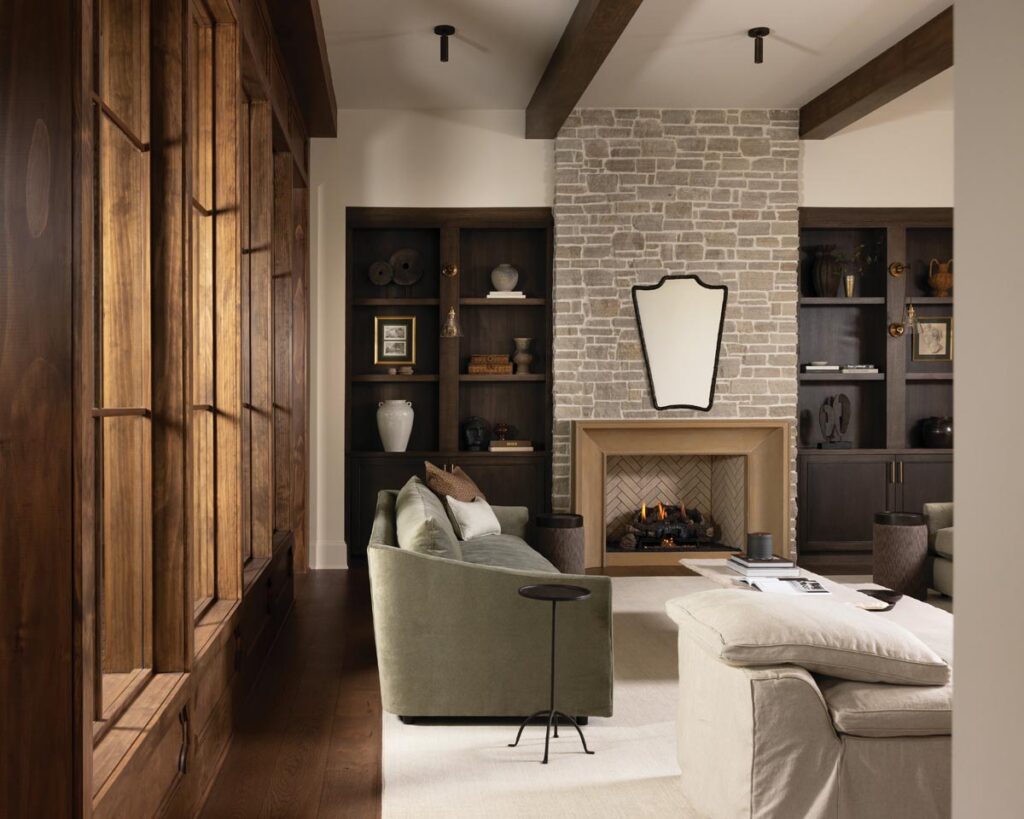 The furnishings and materials in the living room create warmth and intimacy while allowing the natural light and sight lines throughout the home to remain the focus. The fireplace surround was fabricated from a precast material with a limestone façade. The Champagne Cobble brick above it was selected for its vintage look. Crafted from oak and finished in a rich stain, the built-in shelves display cherished accessories, books, and mementos.