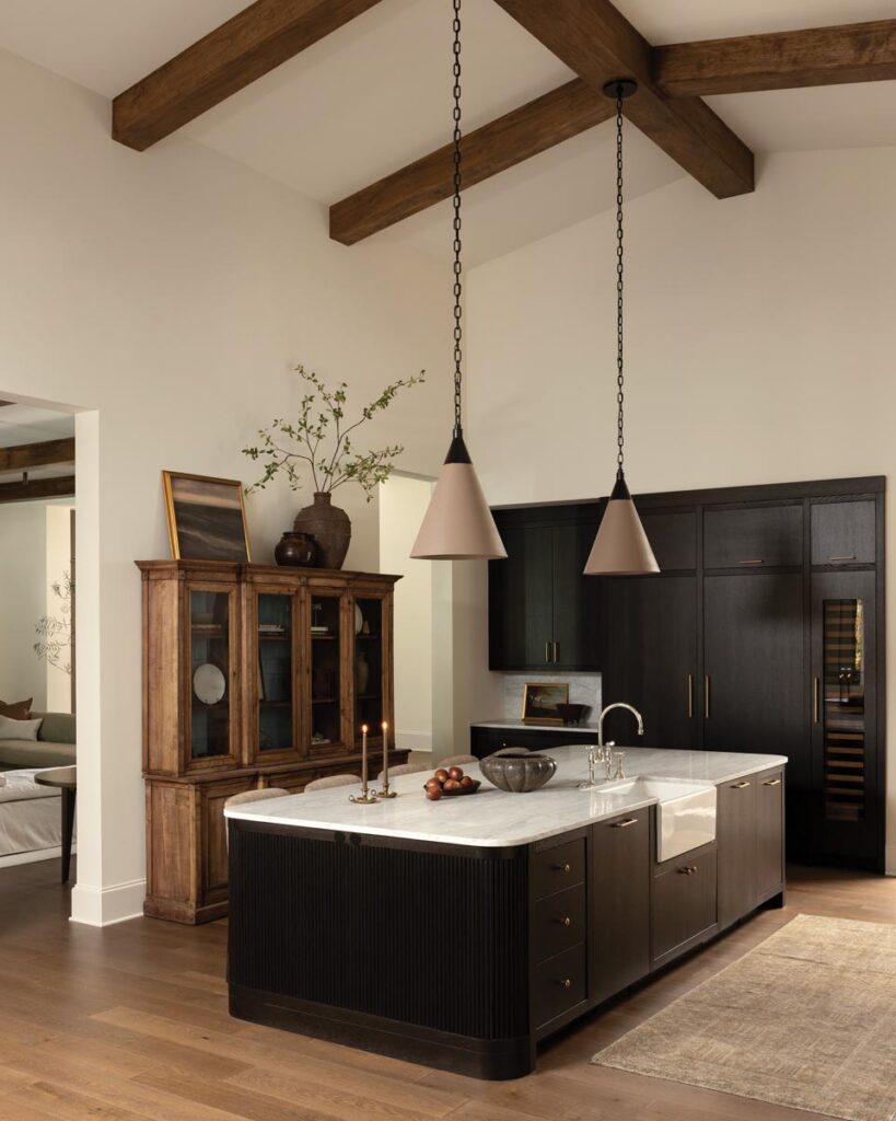 The kitchen features custom stained-oak cabinetry designed to feel like finely crafted furniture. Integrated appliances and concealed storage maintain a cohesive appearance. The Urban Electric pendants were chosen for their tailored forms, which balance the substantial scale of the island.