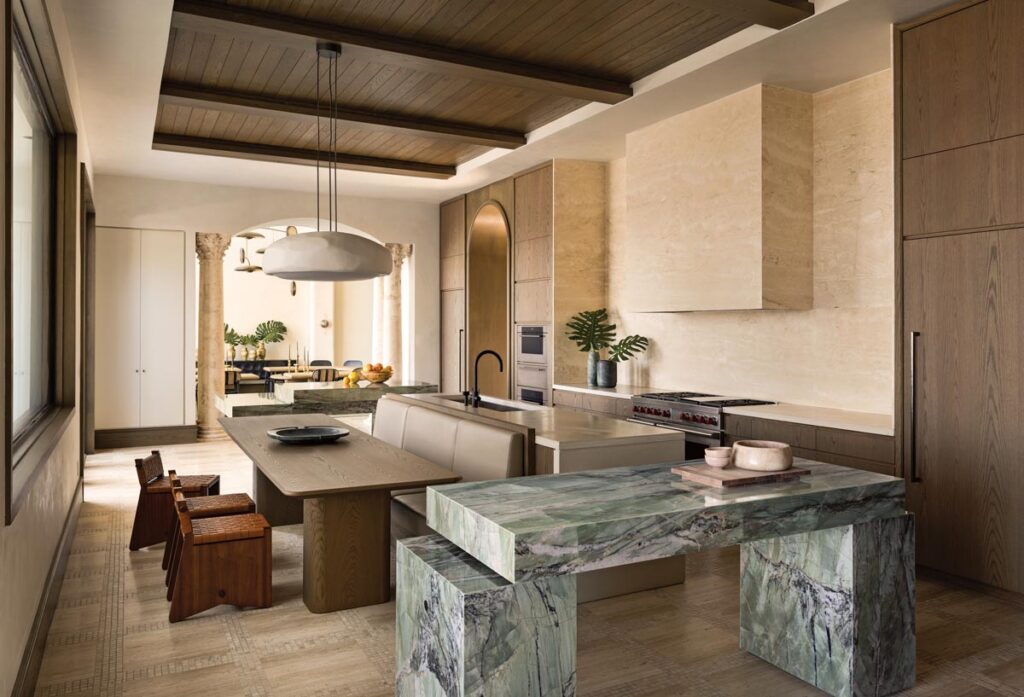 “The kitchen was challenging to design because it’s a very long room that needed to satisfy the demands of a family that enjoys cooking and entertaining,” says designer Abraham Chan. “We decided to anchor the sides of the space with two sculptural green quartzite islands that act as serving tables. The cypress wood ceiling balances the monolithic travertine expression of the kitchen.”