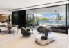 Miami Beach Home is An Unfolding Design Story The residence’s ground floor ceiling peaks at over 20 feet, then eases into a more intimate plane as you move toward the water. Floor-to-ceiling black steel sliding panels retract completely, dissolving indoor/outdoor boundaries. Sleek Minotti furnishings include a low-slung ivory sofa, sculptural swivel chairs, and a reflective glass-and-bronze cocktail table.