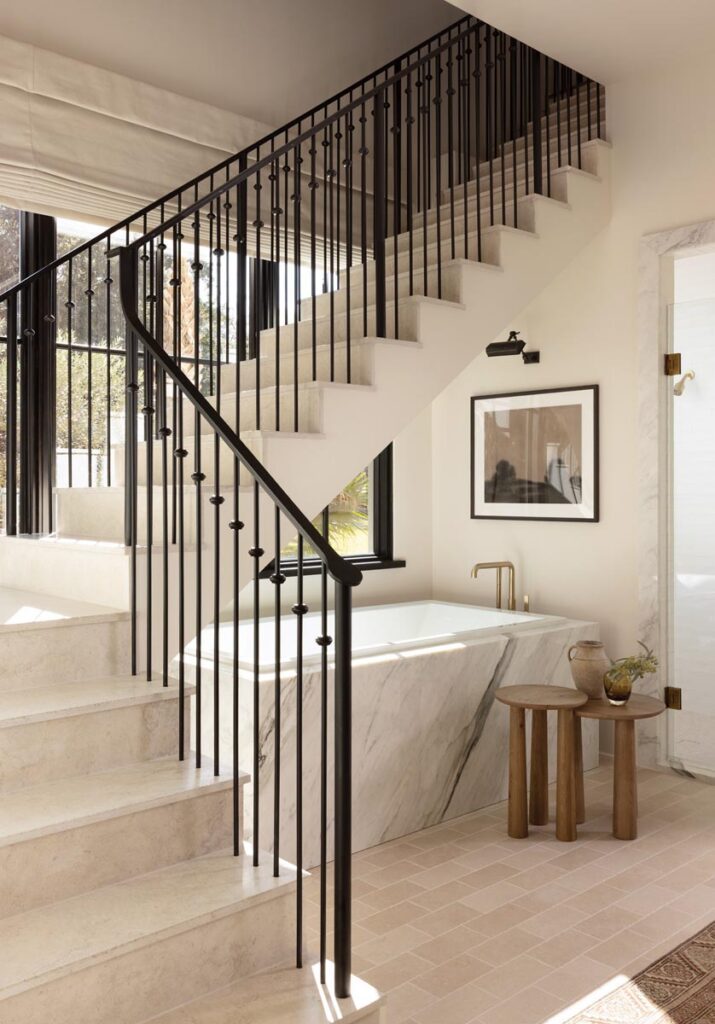 The unusual placement of a staircase inspired the design team to treat the primary bathroom as a sculptural, spa-like environment organized around the tub. The result is an unexpected architectural moment that feels dramatic yet serene.