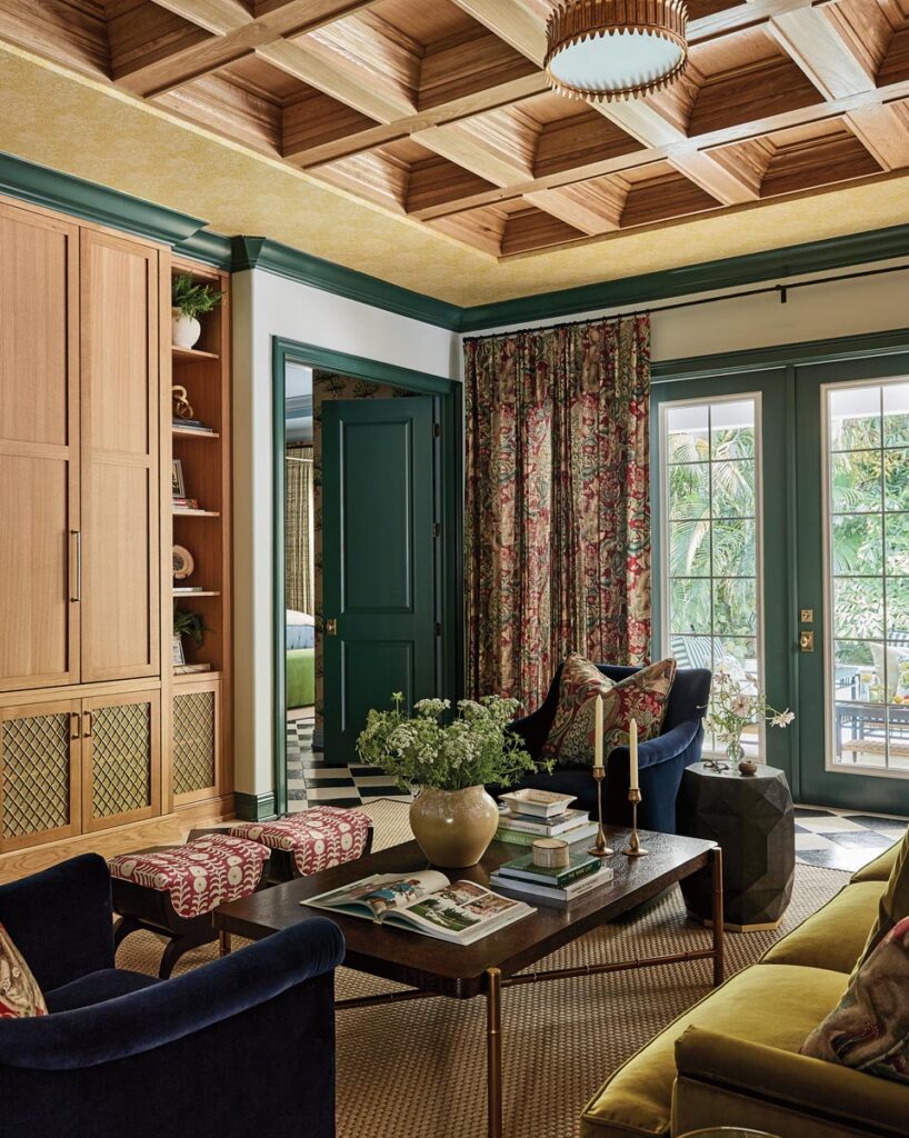 A coffered ceiling in a honey oak stain warms the living room, which is layered in deep jewel tones of navy, chartreuse, and red. Fine textiles, including mohair and velvet, cover a sofa, club chairs, and an ottoman, all from Hickory Chair.