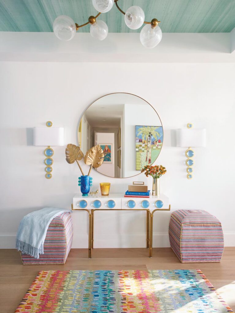 A console and sconces by Jonathan Adler catch the eye in the foyer, which sets the tone for the colorful interiors to come. Furnishings here include ottomans by Ammon Hickson, a mirror from CB2, a Hudson Valley Lighting chandelier, and an area rug by Dash & Albert.