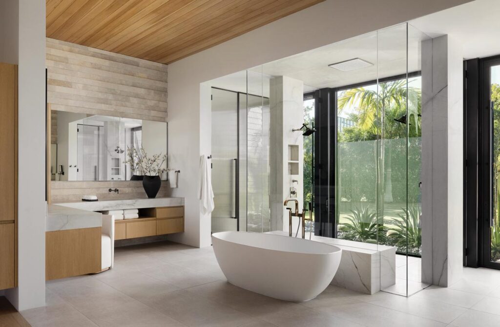 In the primary bathroom, an elegant freestanding Barcelona tub from Victoria + Albert rests near the glass-enclosed shower whose panels can turn opaque for privacy at the touch of a button.