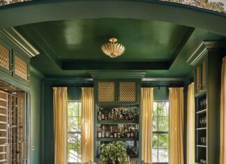 A coffered ceiling brings architectural interest to the library, along with built-in shelving that arches over a mint green sofa from Rowe and a custom upholstered ottoman. A Pierre Frey mural wallpaper continues from the hallway, adding a rich layer of pattern.