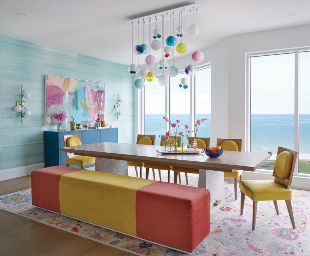 The custom Boffi chandelier in the dining room perfectly encapsulates the playful spirit of the residence, and its colors are echoed by the other furnishings, including a custom-made yellow and orange bench, a blue buffet by Hammer Fine Furniture, and an abstract artwork. A rug by FJ Kashanian and wallcovering by Phillip Jeffries add to the palette.
