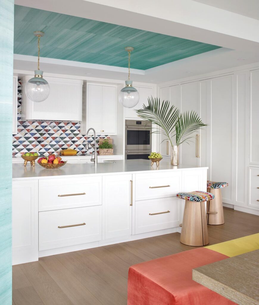 “We used the kitchen as a neutral anchor point within the home, giving the eye a place to rest from the more saturated colors throughout the condo,” says Gaddis. All-white cabinetry is the ideal contrast to the aqua ceiling covering by Phillip Jeffries and backsplash with mosaics from Artistic Tile.